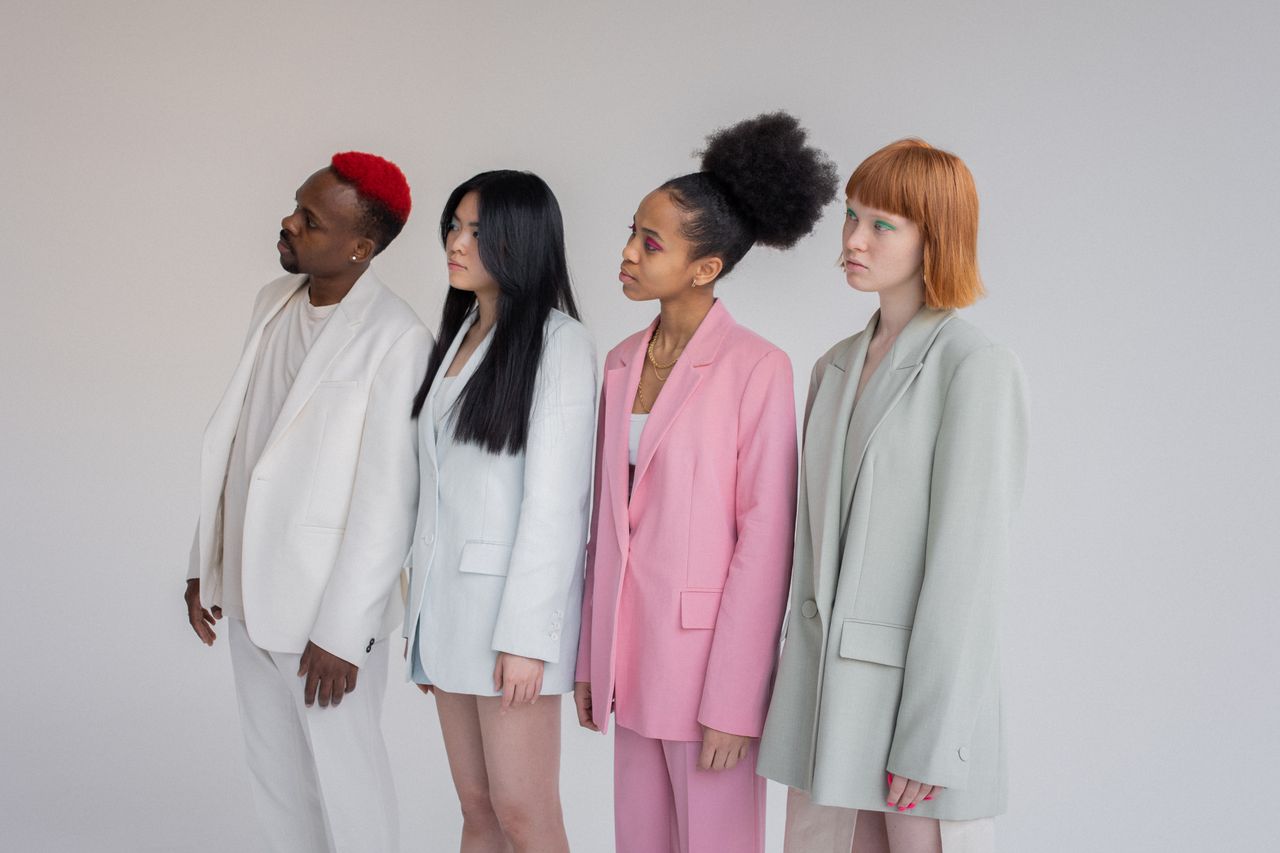 mobile-02 Multiethnic female models and man wearing elegant outfits standing in line against gray background and looking away with attention